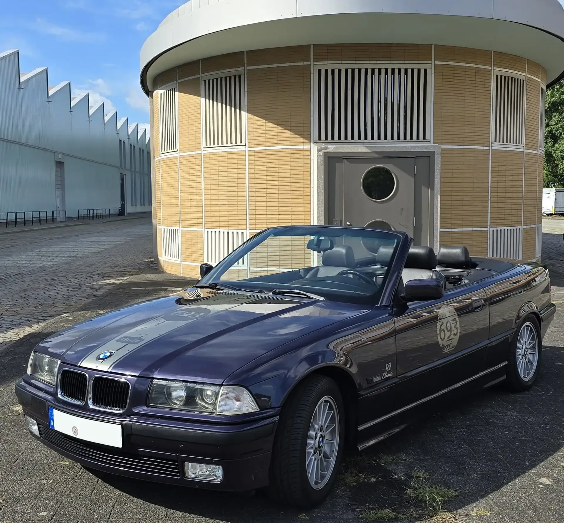 Blauer Oldtimer mit dezenter Beschriftung vor einem Rundbau