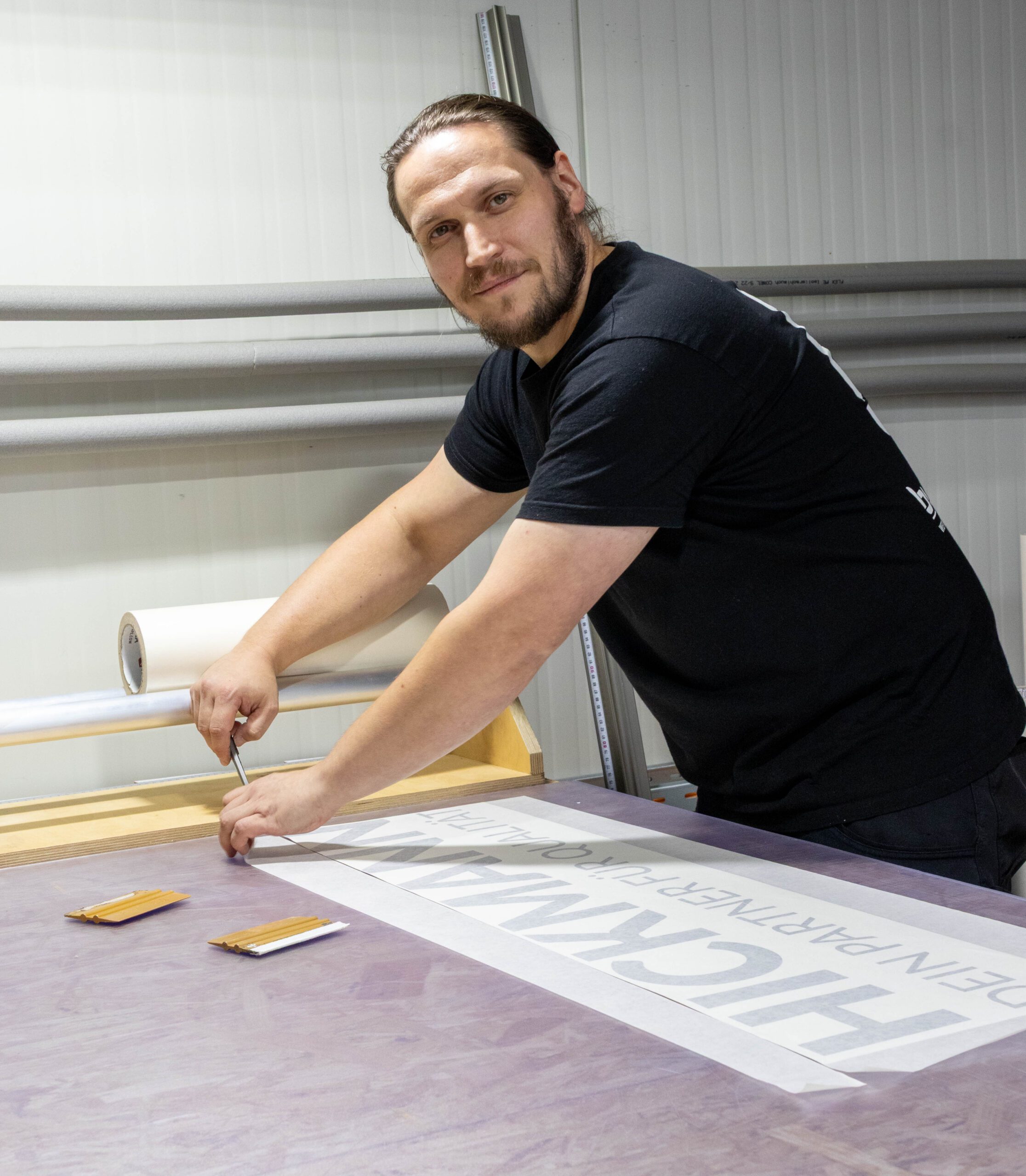 Sebastian Bock von buzzdesign beim Zuschneiden einer Folienbeschriftung in der Werkstatt.
